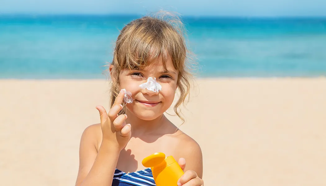 Girl at beach putting on sunscreen.