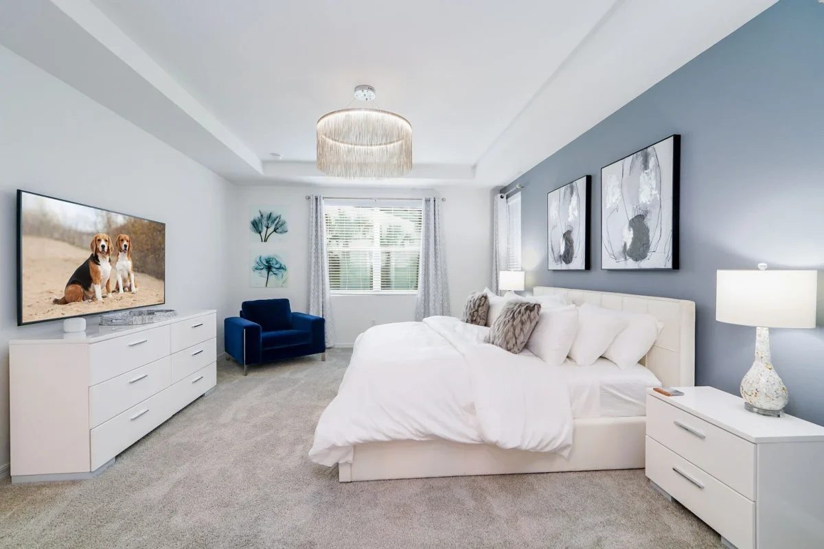 Bright master bedroom in an Orlando vacation rental featuring a king bed, wall-mounted TV, modern décor, and peaceful neutral tones in a Central Florida home near Disney. 