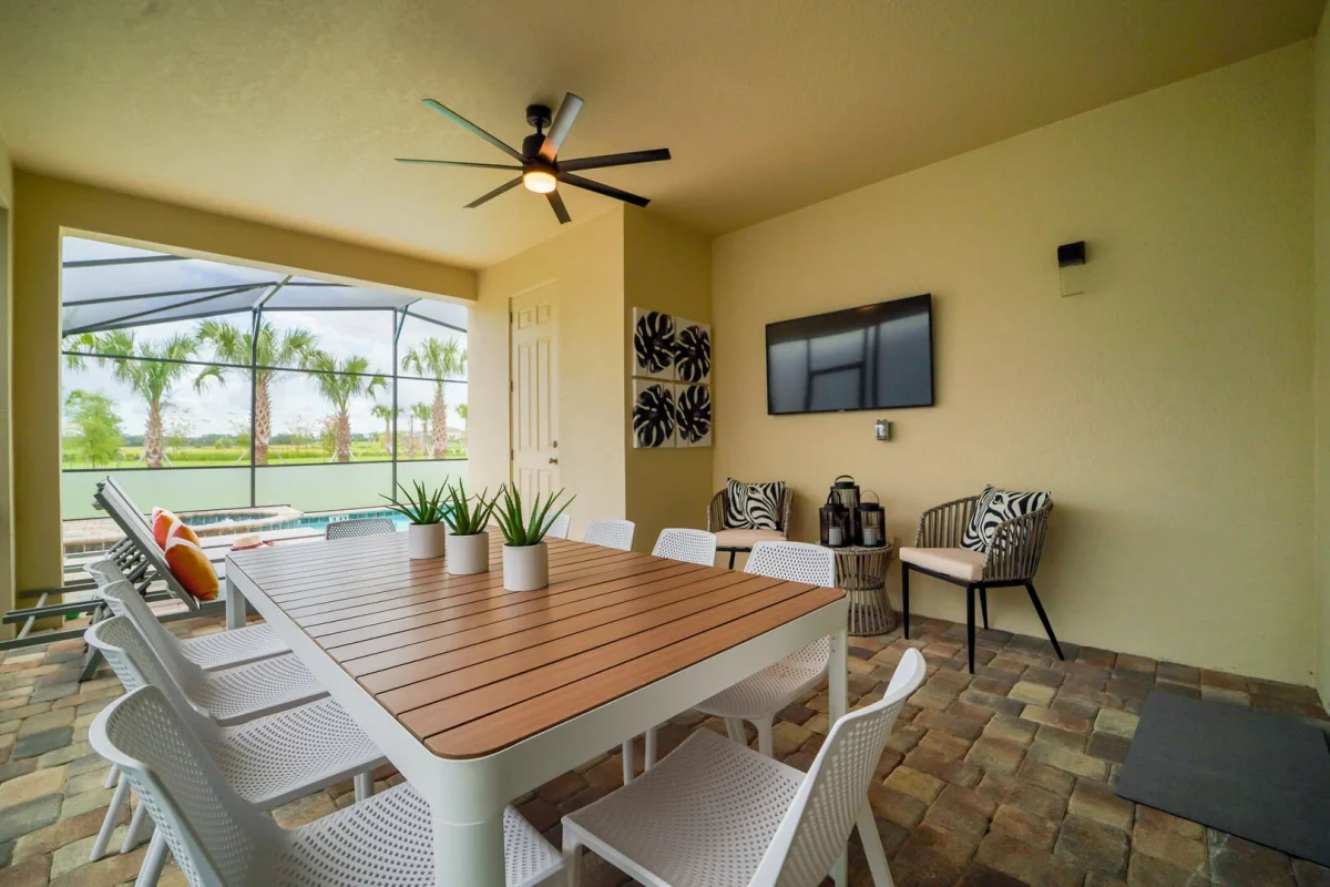 Covered outdoor patio with dining table, seating area, ceiling fan, and TV overlooking a screened private pool at an Orlando vacation rental in Central Florida.