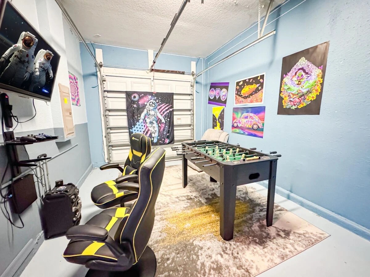 Garage game room in an Orlando vacation rental featuring a foosball table, gaming chairs, wall-mounted TV, and colorful space-themed décor-perfect for family-friendly stays near Disney.