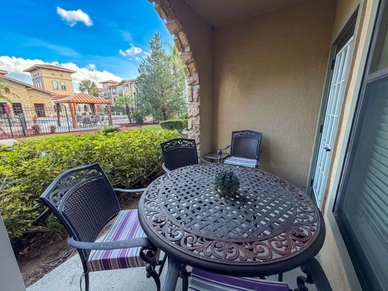 Private covered patio with outdoor table and chairs overlooking landscaped grounds and resort pool area. 