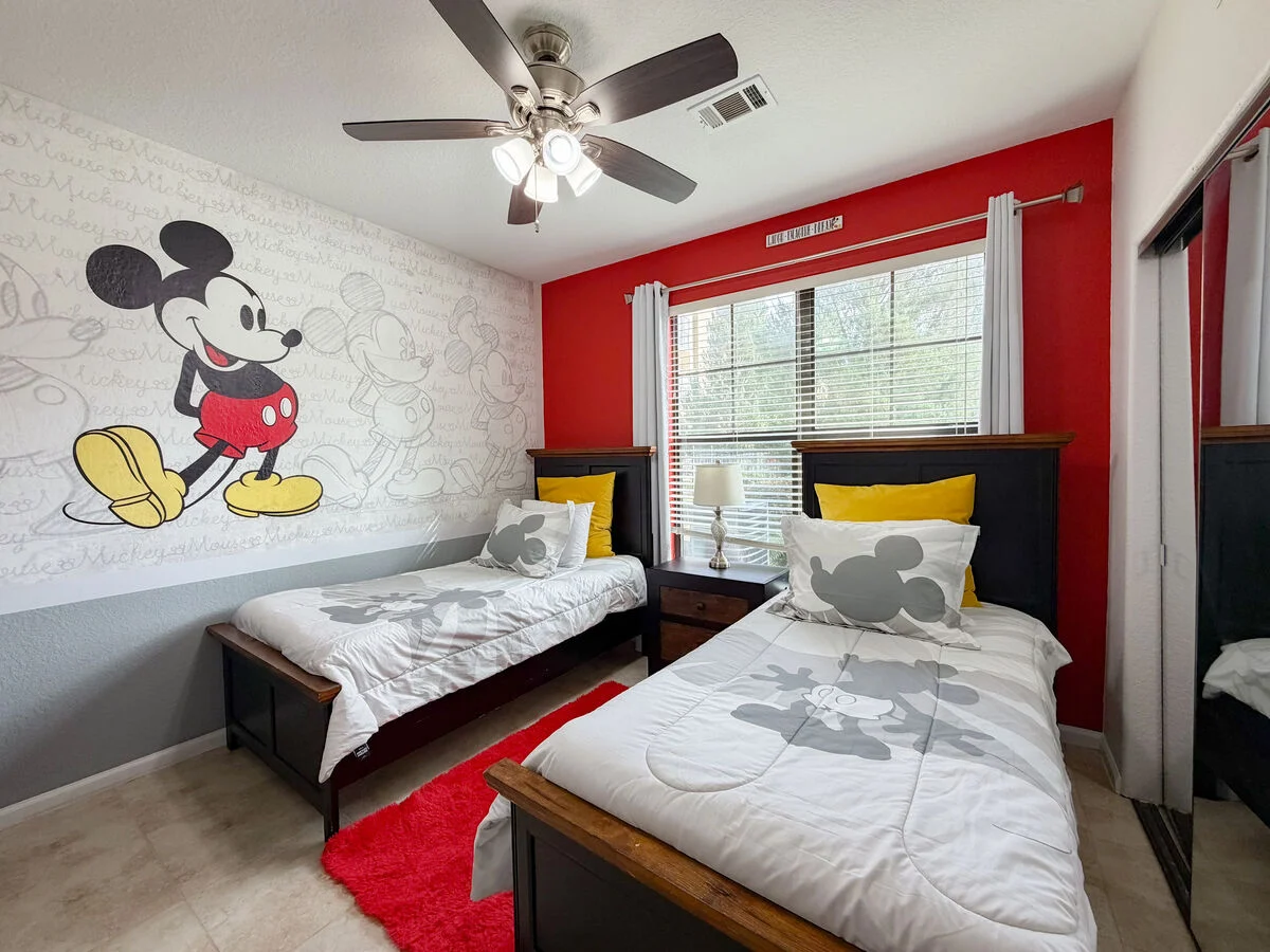 Themed kids bedroom with two beds, character wall mural, ceiling fan, and bright red accent wall.