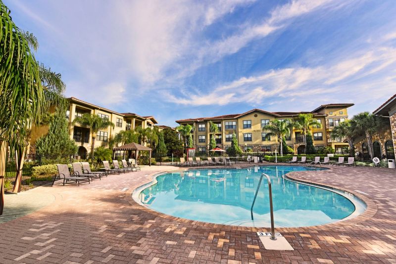 Resort style community pool surrounded by lounge chairs and condominium buildings with palm trees.